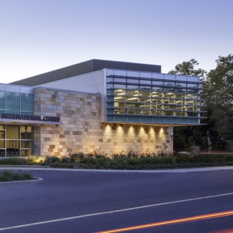 Modern international center building with a glass-fronted upper level, lit stone facade, and road in front at dusk