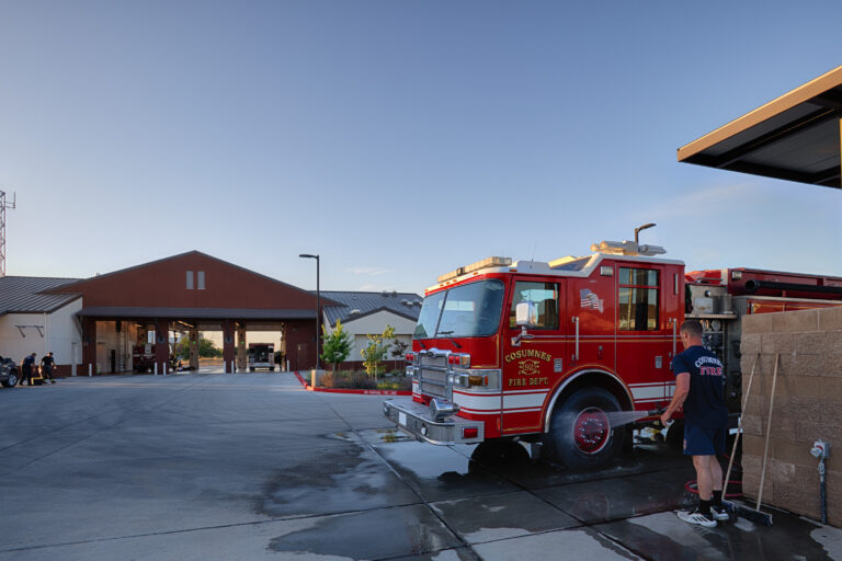 Firefighter washing a red Cosumnes Fire Department truck outside a fire station at sunset