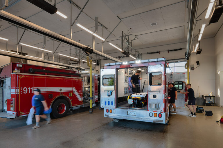 Firefighters and paramedics prepare an ambulance beside a red 911 fire truck inside a station garage.