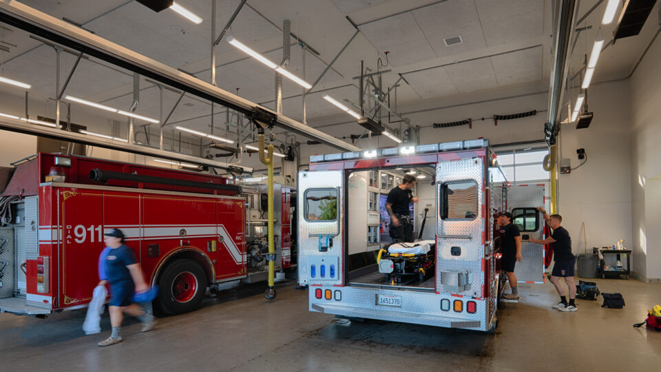 Firefighters and paramedics prepare an ambulance beside a red 911 fire truck inside a station garage.