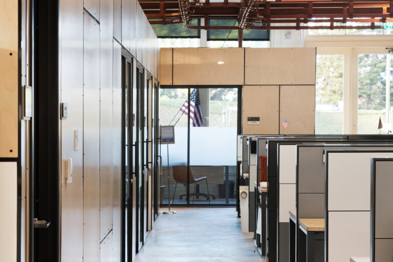 Modern office hallway with cubicles, wood-paneled walls, and exposed industrial ceiling beams