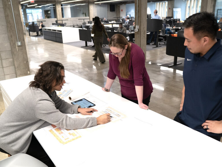 Three coworkers reviewing plans together at a table in a modern open office.