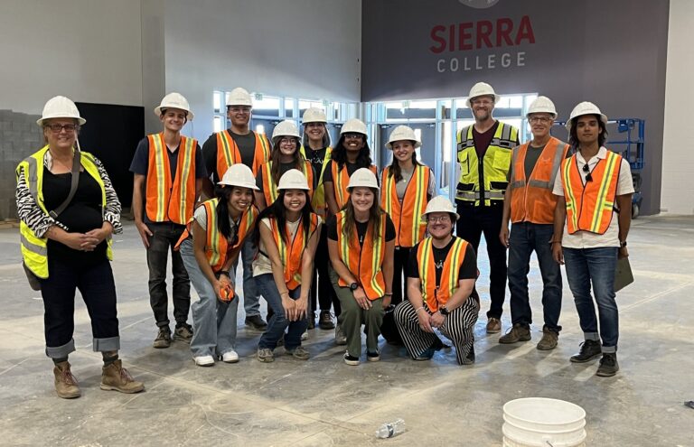 Group of students and staff in hard hats and safety vests inside a building under construction at Sierra College