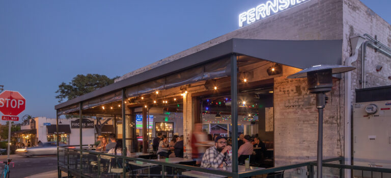 Outdoor restaurant patio at dusk with diners under string lights and a glowing FERNside sign on the roof
