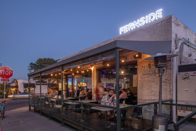 Outdoor restaurant patio at dusk with diners under string lights and a glowing FERNside sign on the roof