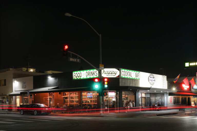 Nighttime street corner at 30th St with a lit cocktail bar, traffic lights, and red car light trails.