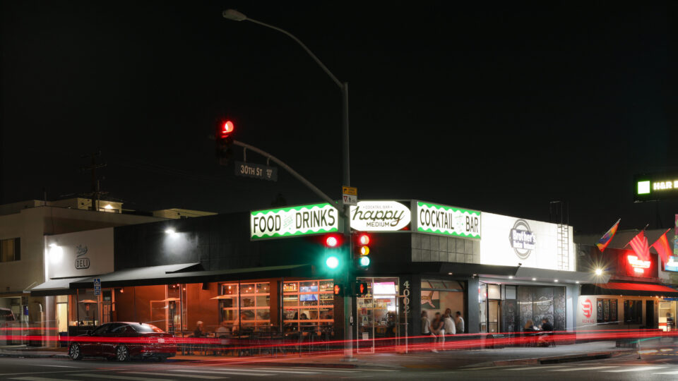 Nighttime street corner at 30th St with a lit cocktail bar, traffic lights, and red car light trails.