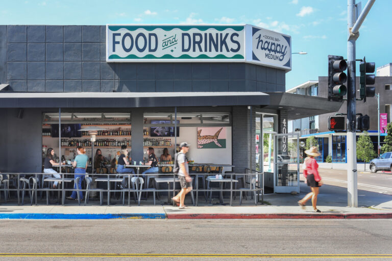 Street-corner bar with open seating and patrons, beneath signs reading Food and Drinks and Happy Medium cocktail bar