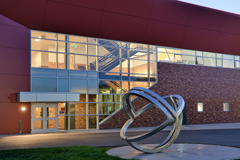 Modern brick building with large glass windows at dusk and an abstract metal ring sculpture in front