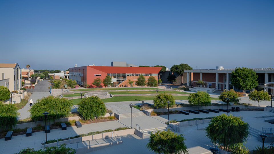 Wide view of a landscaped campus courtyard with walkways, trees, and modern academic buildings under a clear blue sky