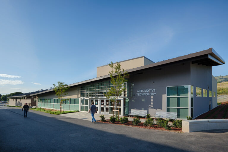 Modern building labeled Automotive Technology with two people walking outside on a sunny day