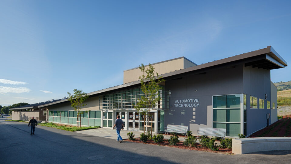 Modern building labeled Automotive Technology with two people walking outside on a sunny day