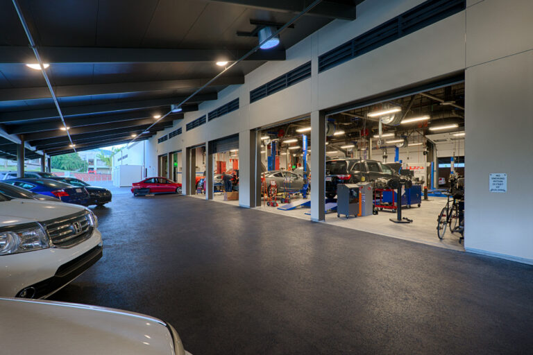 Covered auto repair bay with several cars parked outside and inside under bright industrial lighting