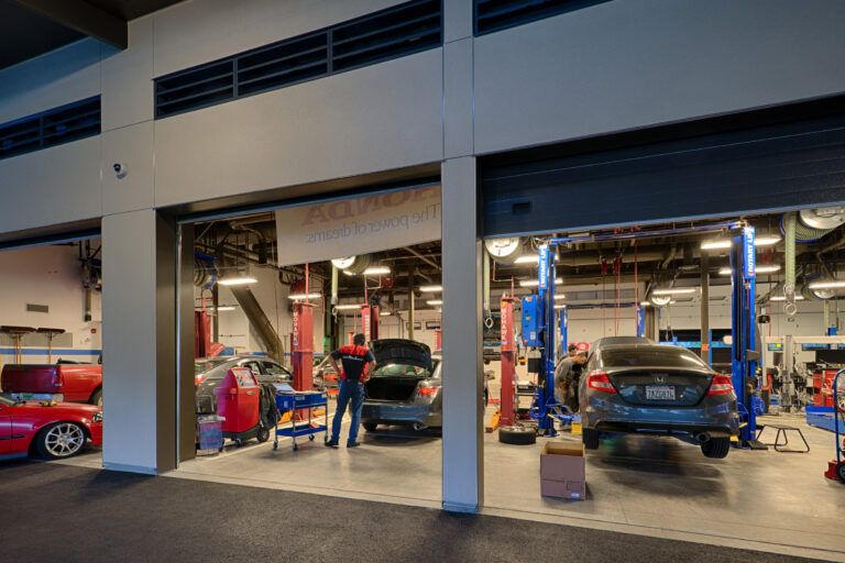 Auto repair shop with several cars in service bays, mechanics working, and one car lifted on a hoist