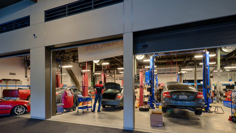 Auto repair shop with several cars in service bays, mechanics working, and one car lifted on a hoist