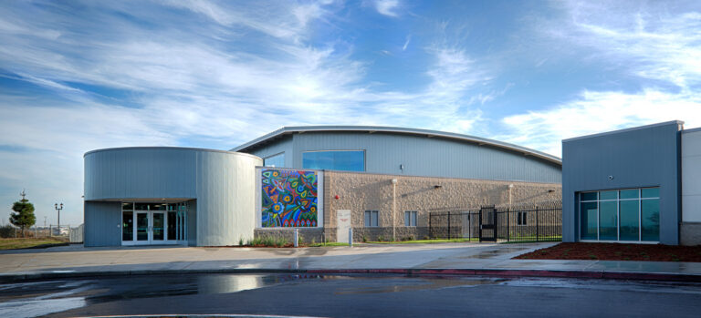 Modern building with curved metal roof, colorful mural, and glass entrance under a blue sky
