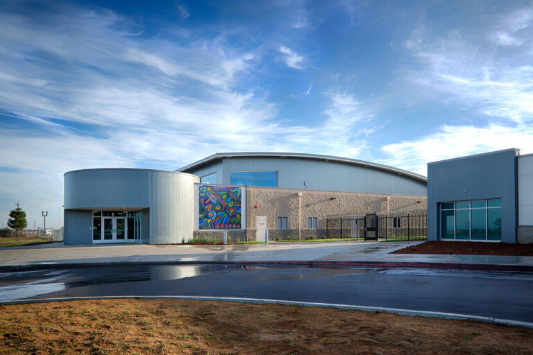 Modern building with curved metal roof, colorful mural, and glass entrance under a blue sky