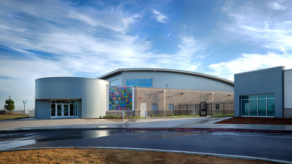Modern building with curved metal roof, colorful mural, and glass entrance under a blue sky