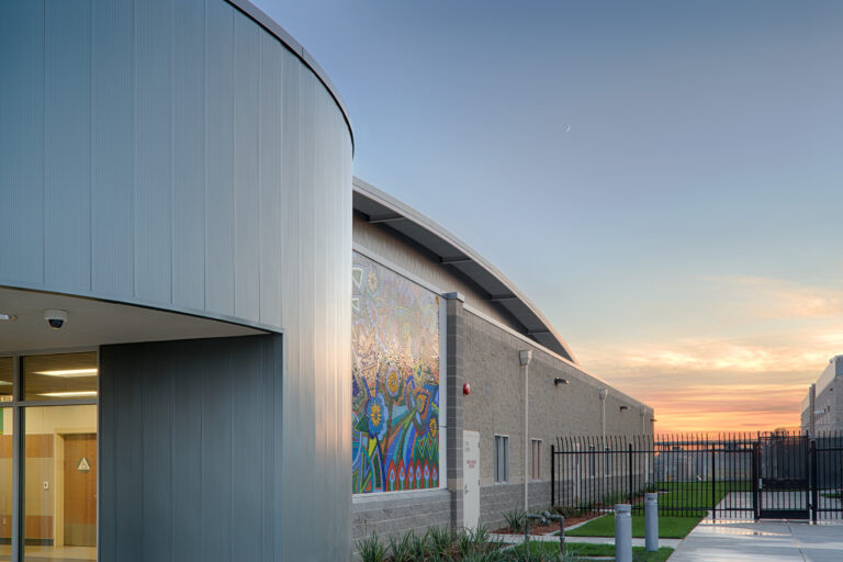 Modern building exterior with a colorful mural, fenced walkway, and sunset sky with a crescent moon