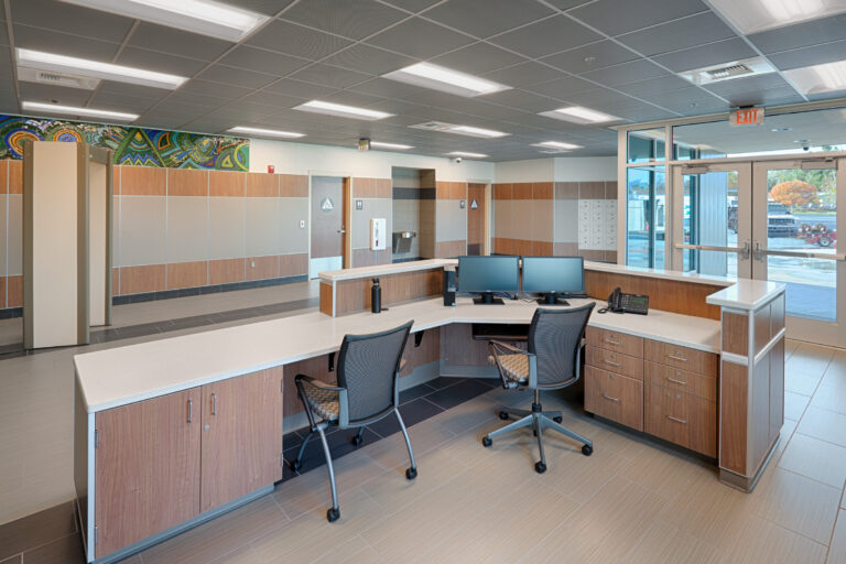 Empty reception desk in a modern office lobby with two chairs, dual monitors, and glass entrance doors