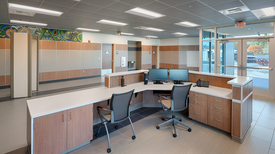 Empty reception desk in a modern office lobby with two chairs, dual monitors, and glass entrance doors