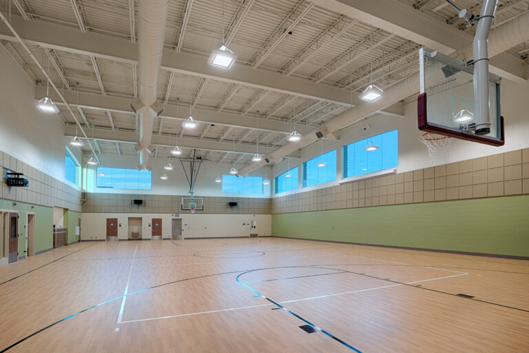 Empty indoor basketball gym with polished wood floors, high ceilings, and multiple hoops