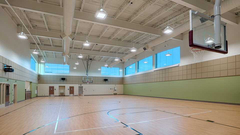 Empty indoor basketball gym with polished wood floors, high ceilings, and multiple hoops