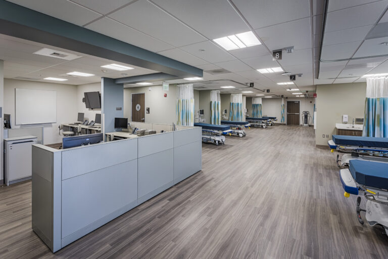 Modern hospital treatment area with numbered bays, curtained beds, and nurses’ stations