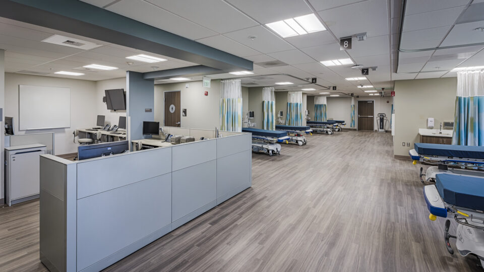 Modern hospital treatment area with numbered bays, curtained beds, and nurses’ stations