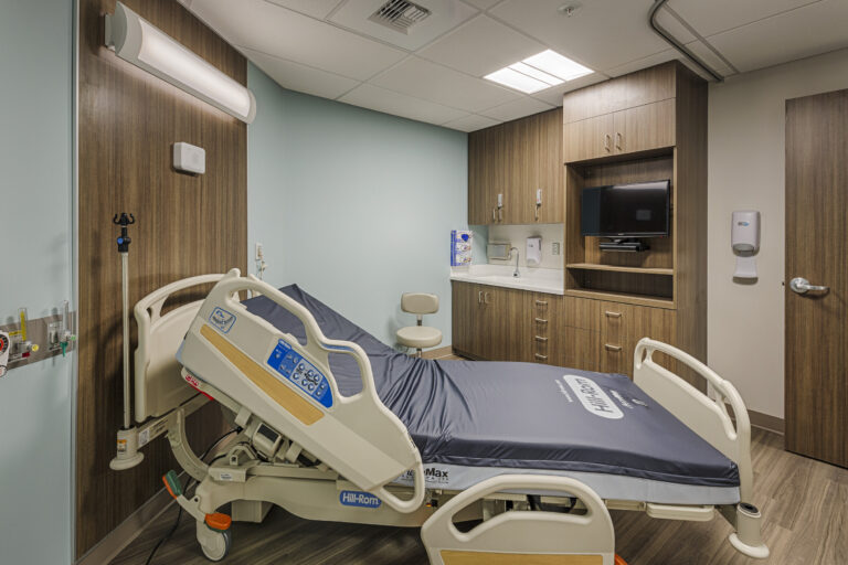 Modern hospital patient room with an adjustable bed, wall-mounted TV, sink cabinet, and medical gas outlets