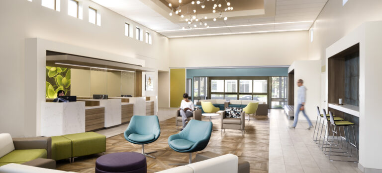 Modern, bright lobby lounge with colorful seating, a reception desk, and people sitting and walking inside