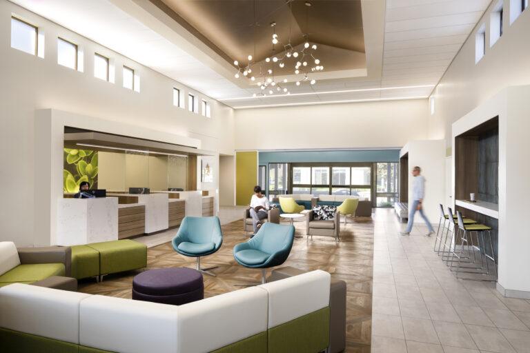 Modern, bright lobby lounge with colorful seating, a reception desk, and people sitting and walking inside