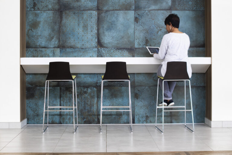 Person sitting on a tall stool using a tablet at a modern counter with blue patterned wall panels