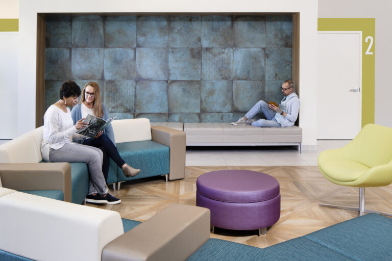 People relaxing in a modern waiting area with colorful seating and a blue tiled wall backdrop