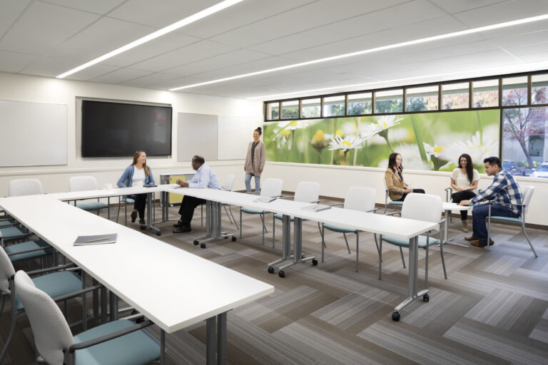 Modern meeting room with people chatting around white tables and a floral wall mural