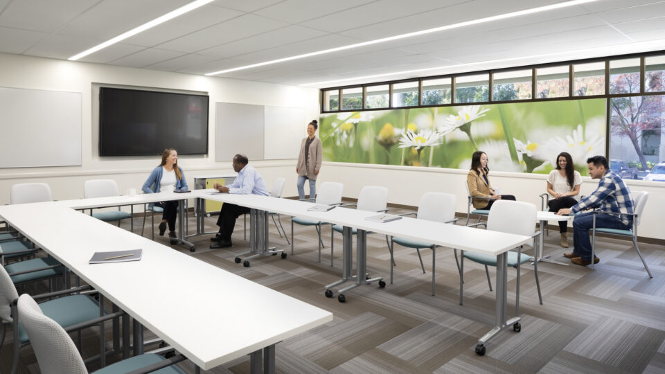 Modern meeting room with people chatting around white tables and a floral wall mural