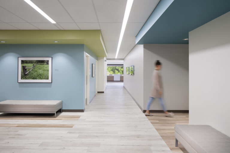 Modern hallway with colorful ceilings, framed art, benches, and a blurred person walking past