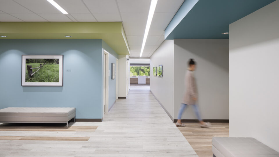 Modern hallway with colorful ceilings, framed art, benches, and a blurred person walking past