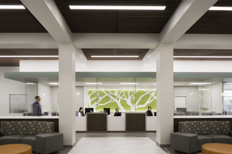 Modern office lobby with reception desks, glass-walled rooms, and people seated behind the counter