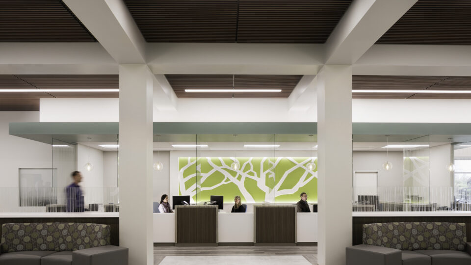 Modern office lobby with reception desks, glass-walled rooms, and people seated behind the counter