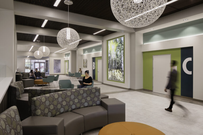 Modern lobby seating area with pendant lights, colorful walls, and people sitting and walking through the space