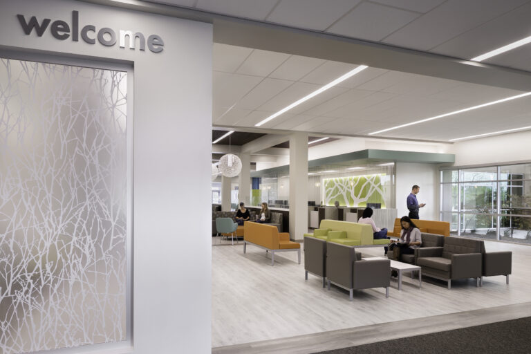 Modern office lobby with a “welcome” sign, colorful seating, and people sitting and standing in a bright open lounge