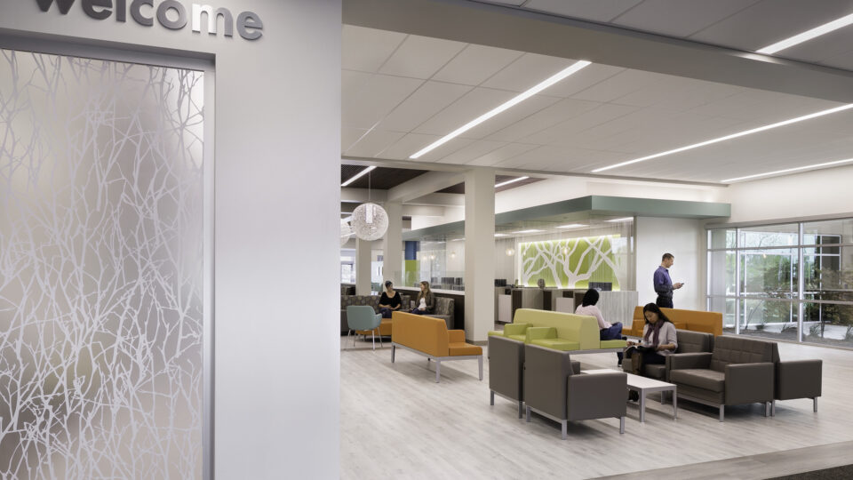 Modern office lobby with a “welcome” sign, colorful seating, and people sitting and standing in a bright open lounge