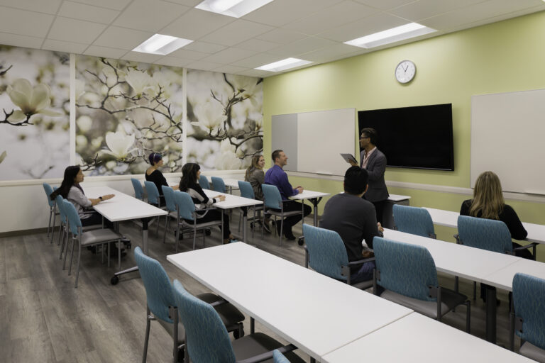 Teacher presenting to students in a bright modern classroom with teal chairs and flower wall murals