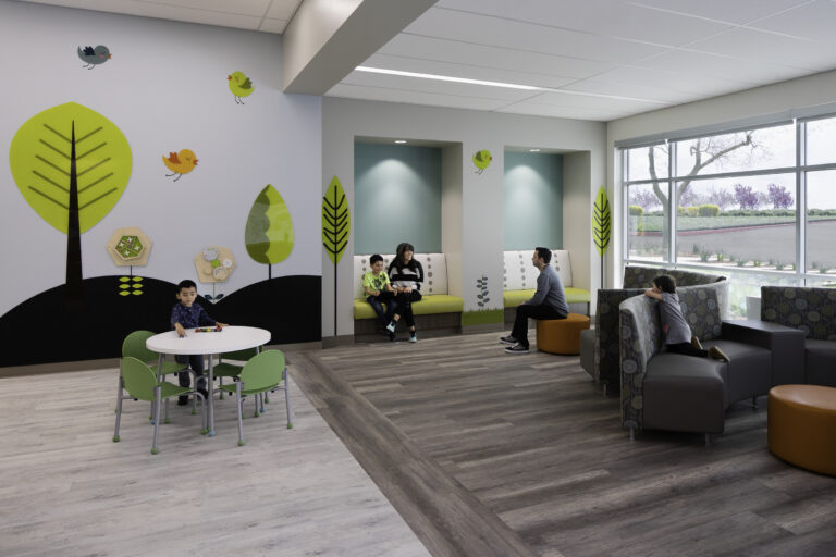 Colorful pediatric waiting room with children and adults sitting on benches and chairs near a play table by large windows