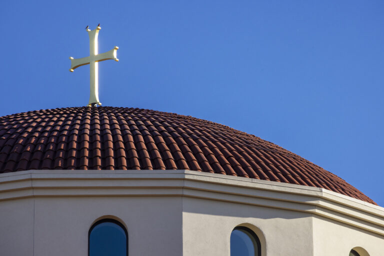 White cross on a red-tiled church roof against a clear blue sky