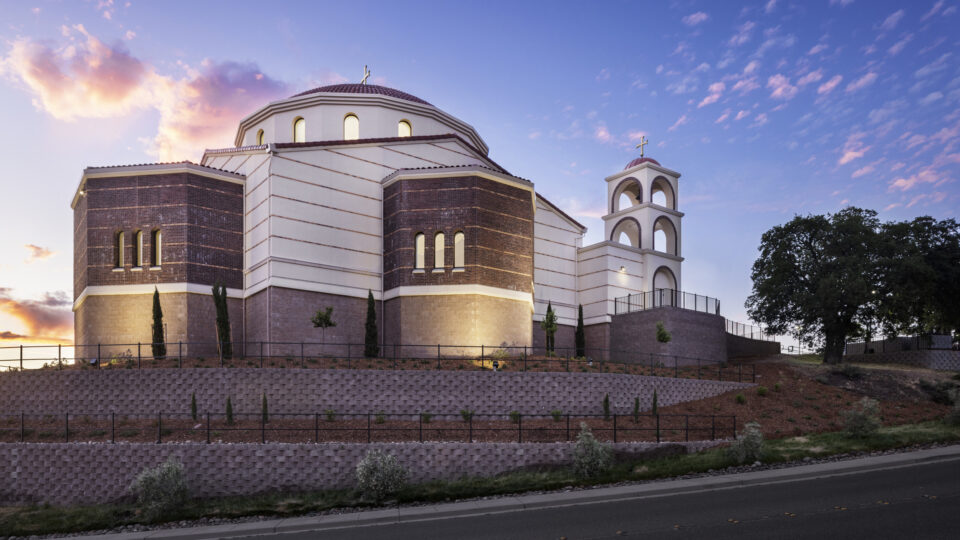A large church with a dome and bell tower at sunset under a pink-blue sky