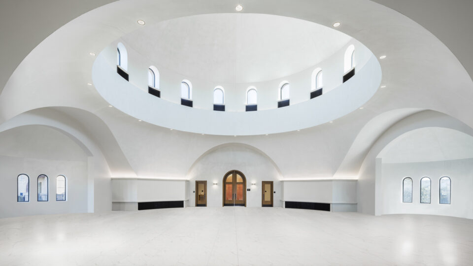 Bright white domed interior with arched windows, a central wooden door, and a large open marble floor