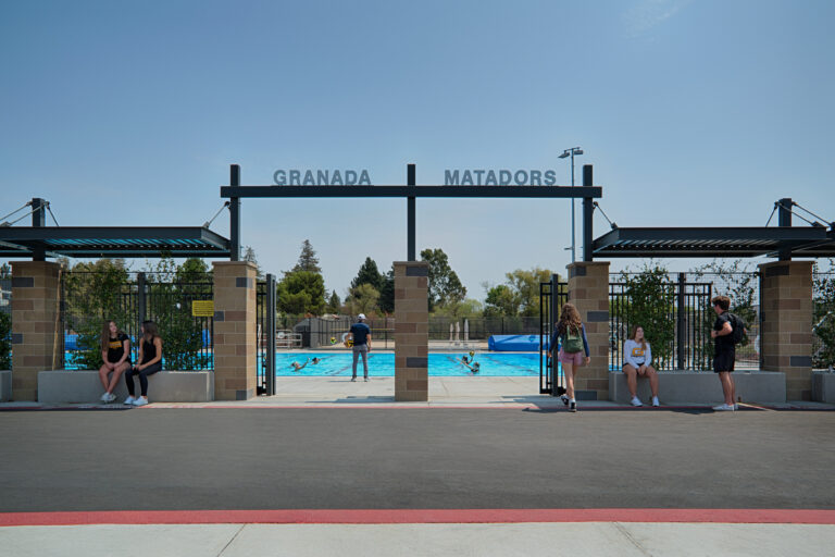 Entrance to Granada Matadors pool with people sitting and walking near the gate under a clear blue sky