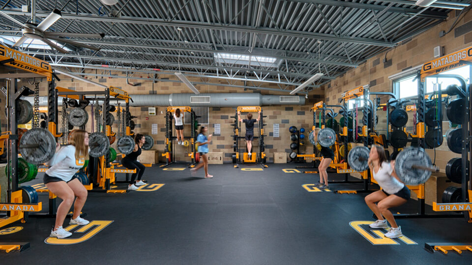 Several athletes perform barbell squats in a weight room with yellow-and-black lifting racks and the word Matadors visible